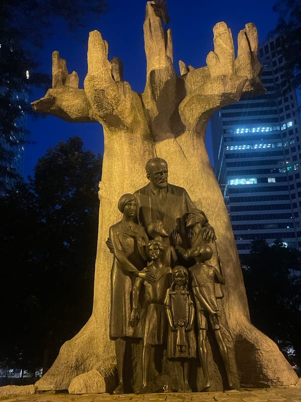 Nighttime plaza scene: fountain, crowd, and bronze statue