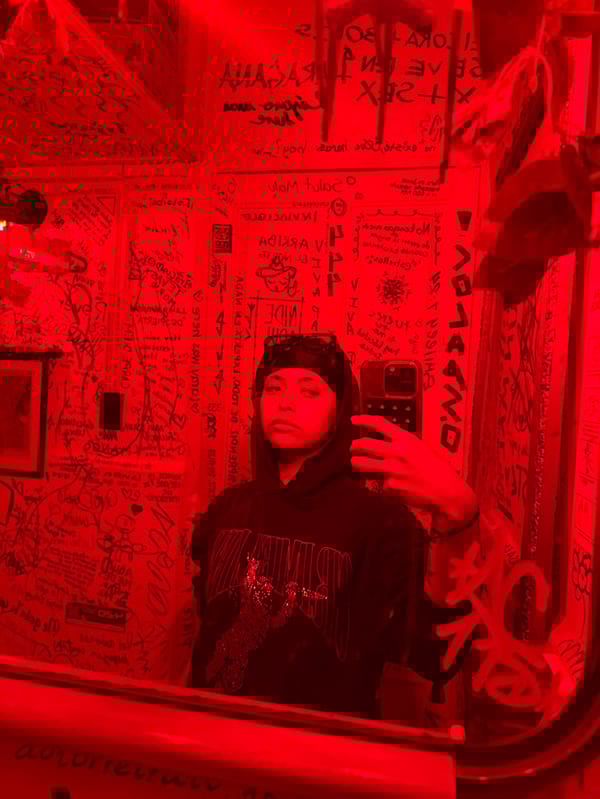 Hooded figure takes mirror selfie in graffiti-covered Mexico City room