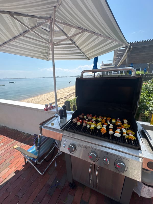 Vegetable skewers on an open barbecue grill under a striped umbrella