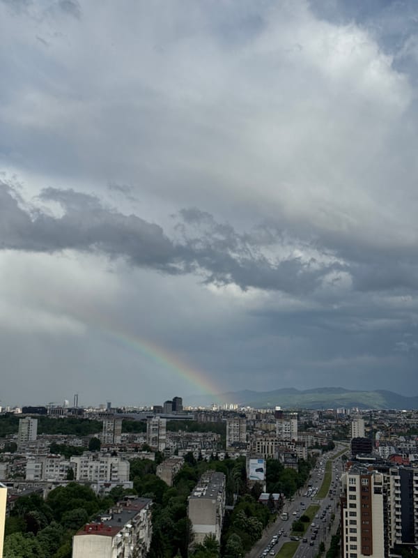 Rainbow appears over dense urban cityscape amid cloudy afternoon