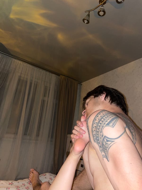 Dimly lit bedroom scene in Minsk, tattoo visible in foreground