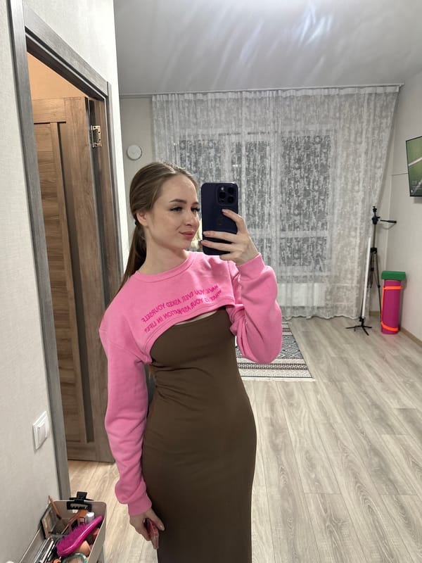 Woman takes mirror selfie in pink top indoors