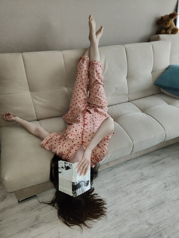 Person lounges in pajamas on sofa, reads newspaper