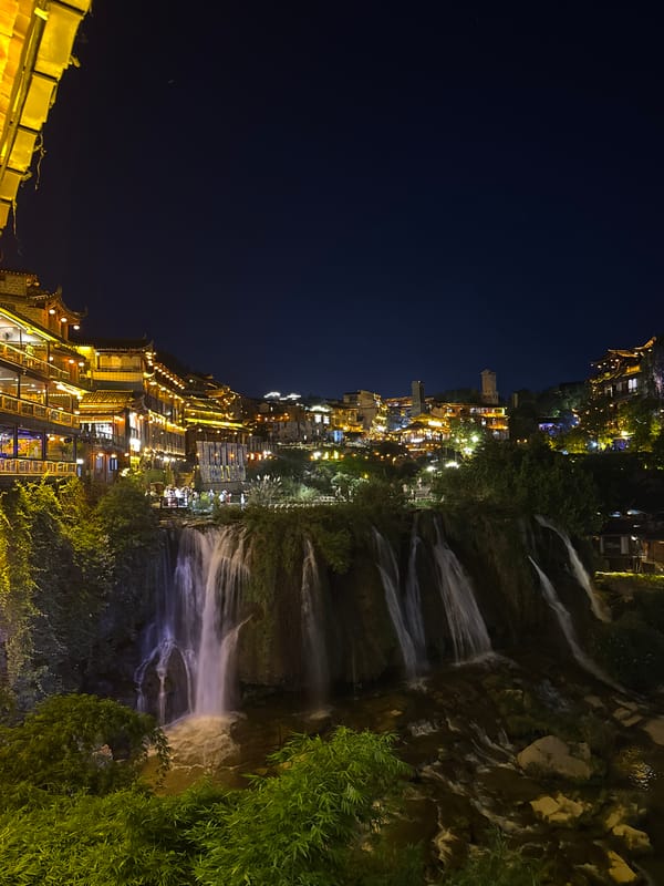 Furong Ancient Town glows at night above its cascading waterfall