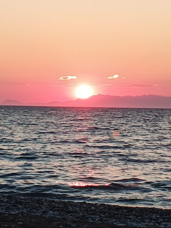 Pebble beach sunset with mountains, pink skies, and calm water