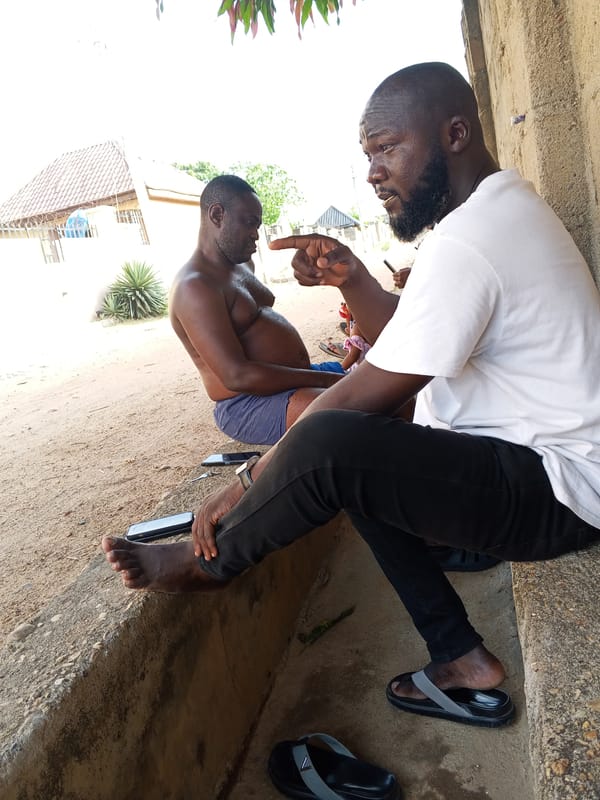 Two men share animated conversation on ledge in Adonkolo