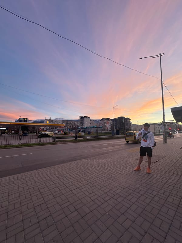 Person observes colorful sunset from city sidewalk