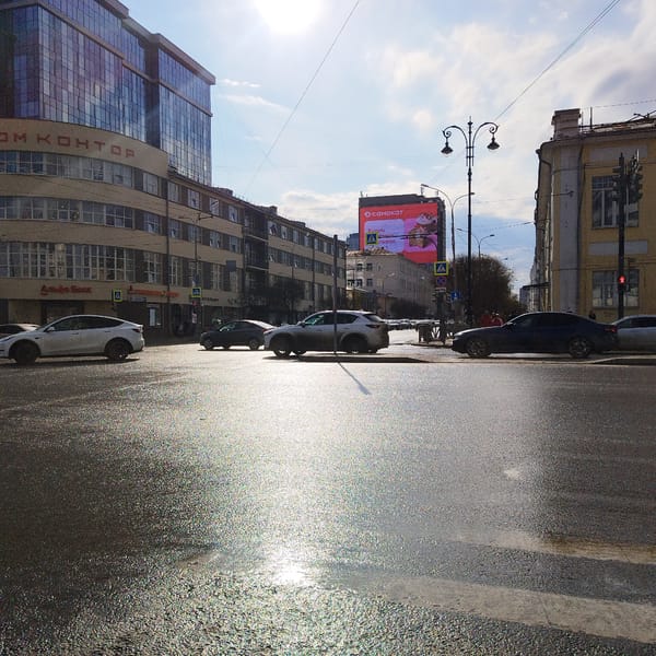 Urban intersection shows wet pavement reflecting bright morning sun