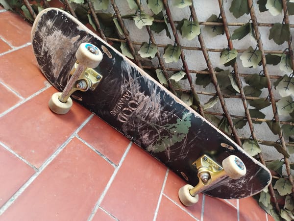 Worn skateboard spotted against wall under partly cloudy skies