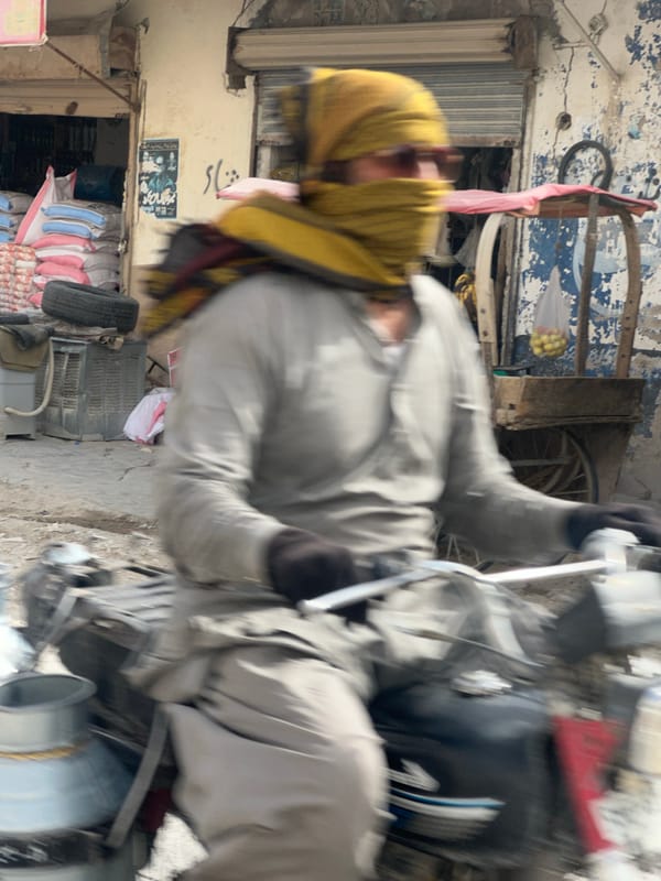 Motorcycle rider navigating Quetta streets, masked and sunglassed.