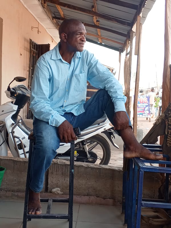 Two men sit outside on stools in Sabon Tasha