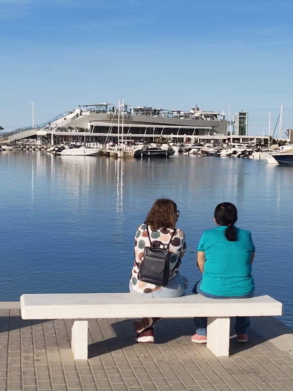 Two women rest on harbor bench in sunny Dénia