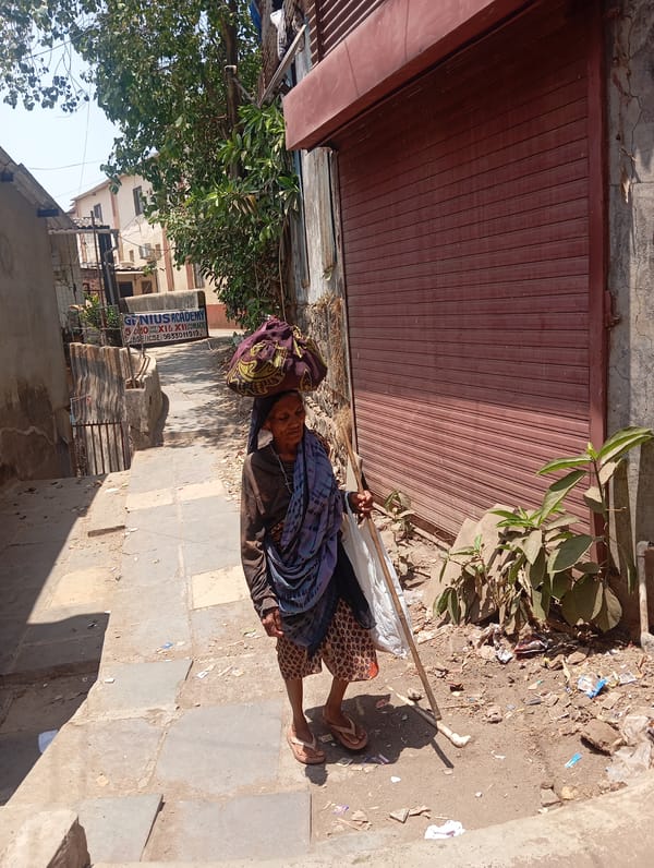 Elderly woman with walking stick navigates Mumbai streets carrying bag