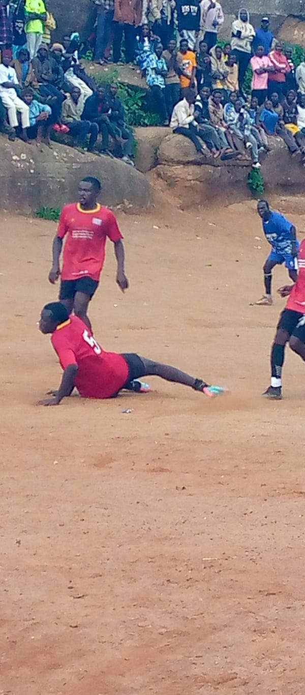 Informal soccer match on a dirt field, crowd on rocky hillside