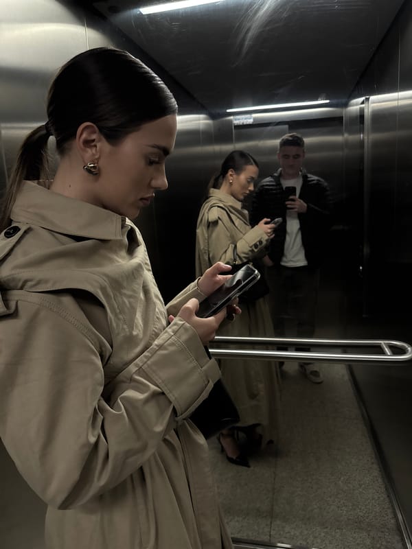 Woman in trench coat uses phone in building hallway