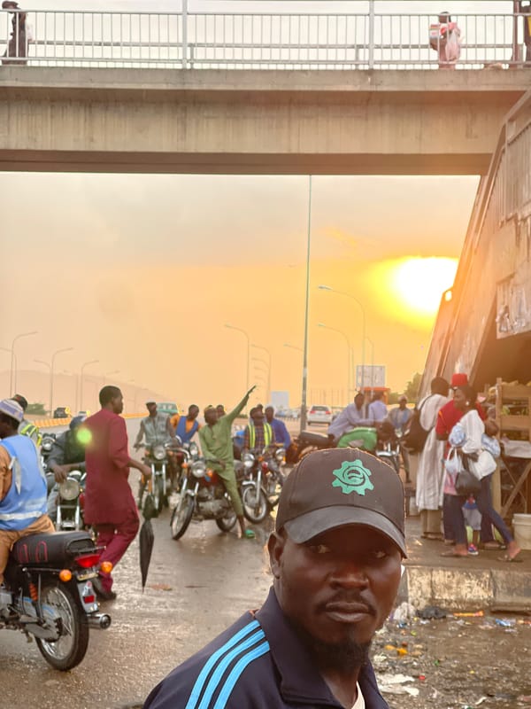 Man poses near motorcycles on busy Gwarinpa street at sunset