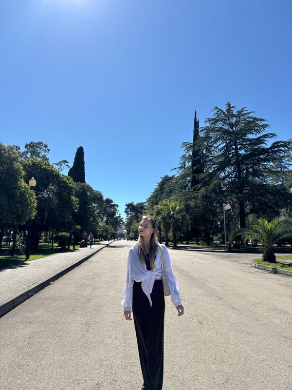 Woman walks tree-lined pathway in Sokhumi under clear skies