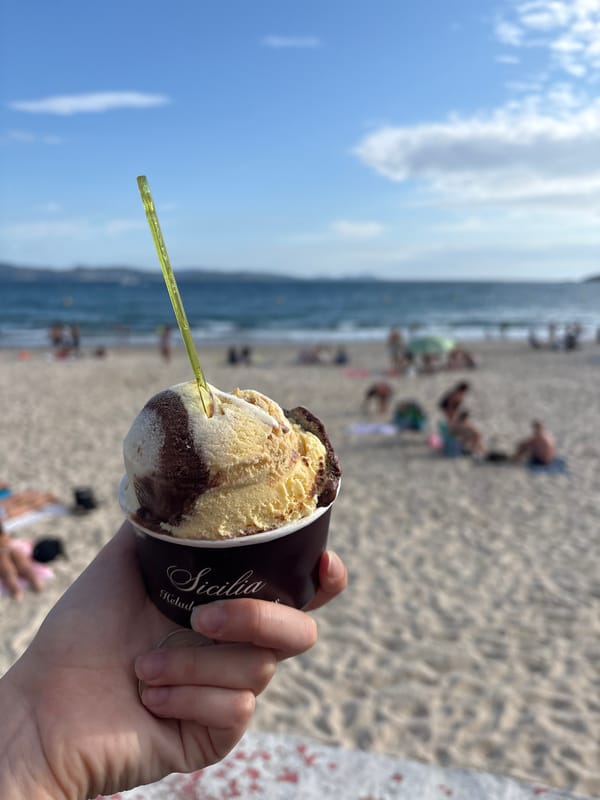 Gelato cup held up against a Sanxenxo beach backdrop
