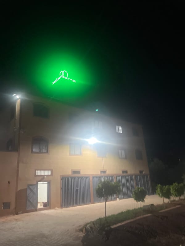 Spotlit building with green neon sign observed in Ouaouizert