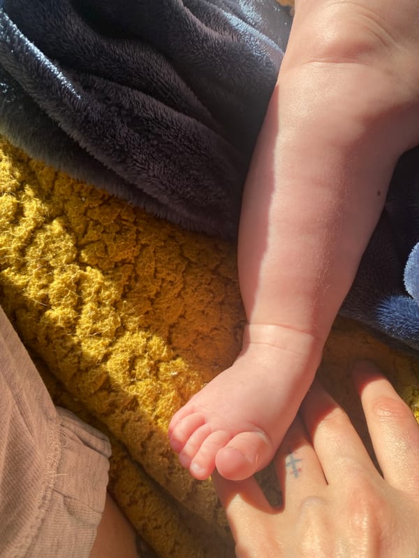 Baby's foot photographed beside tattooed adult hand in Bulgaria