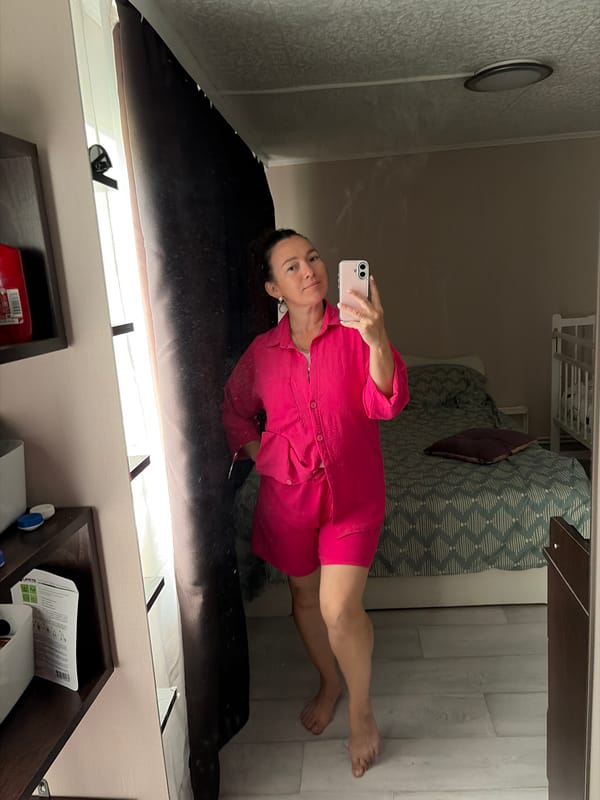Mirror selfie in a pink outfit, bedroom with crib in background