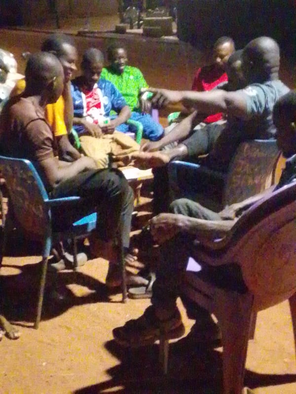 Eight men gather in circle outdoors at night in Tamale