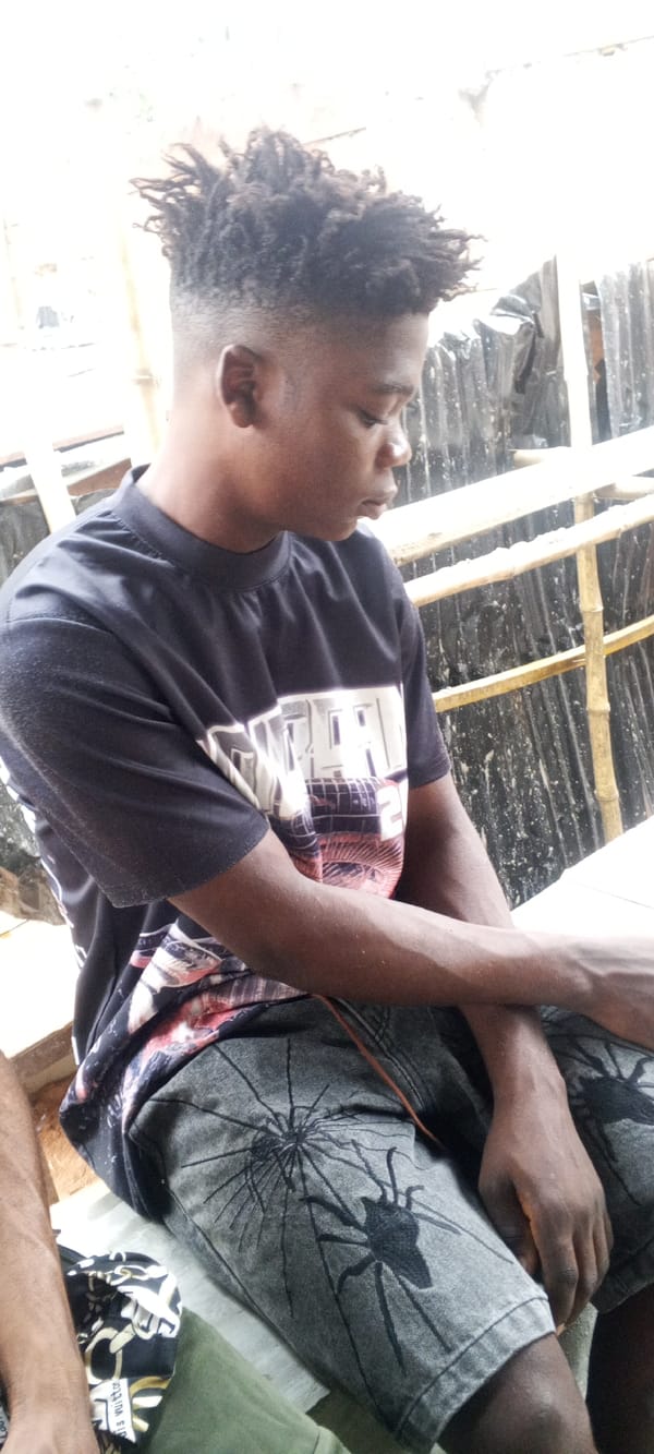 Young man sits quietly in patterned shirt, grey shorts