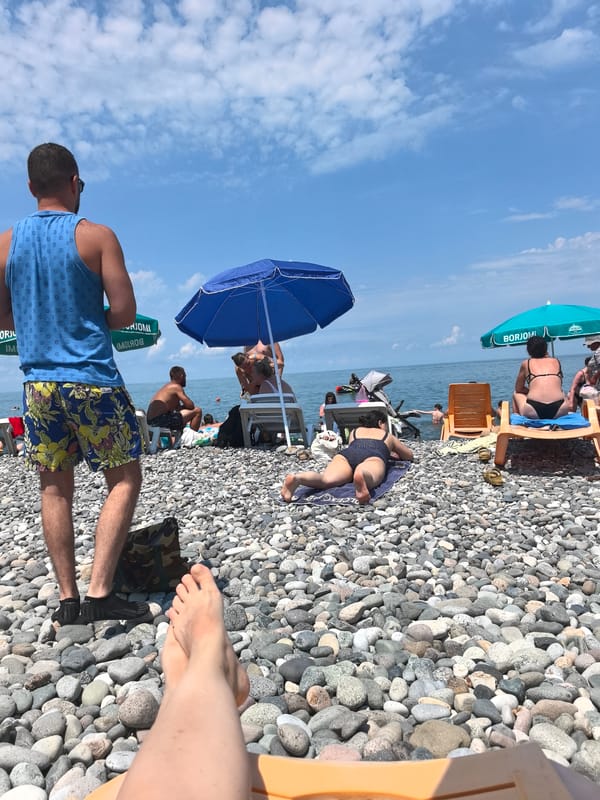 Crowded pebble beach, sunny day, lounge chairs and umbrellas