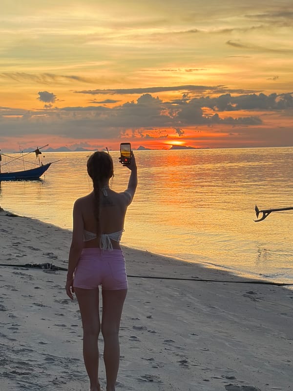 Golden hour on a Thai beach with boats and selfies