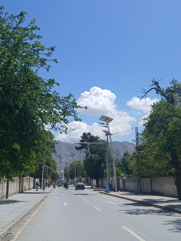 Vehicle travels marked road in Quetta City with pedestrians nearby