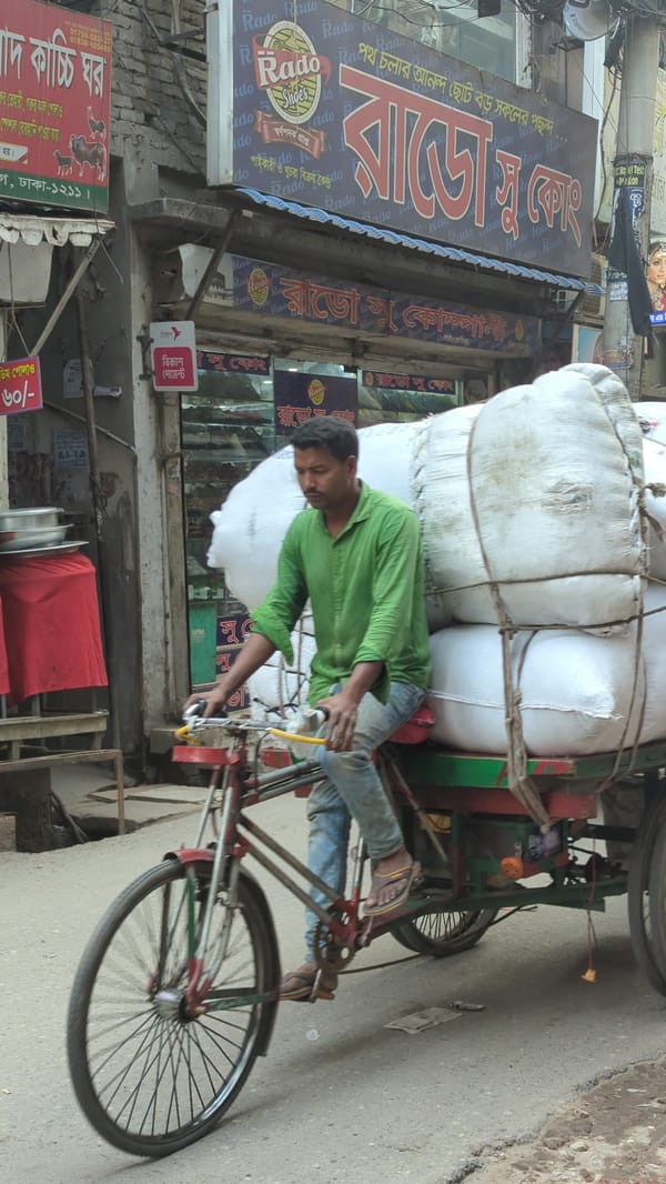 Overloaded rickshaw carries white sacks through Dhaka street