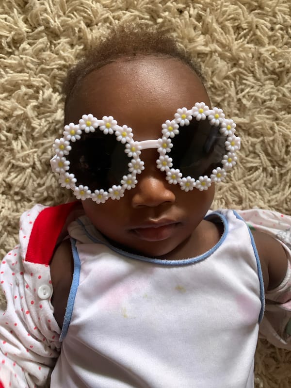 Baby in flower sunglasses photographed on carpet in Nigeria