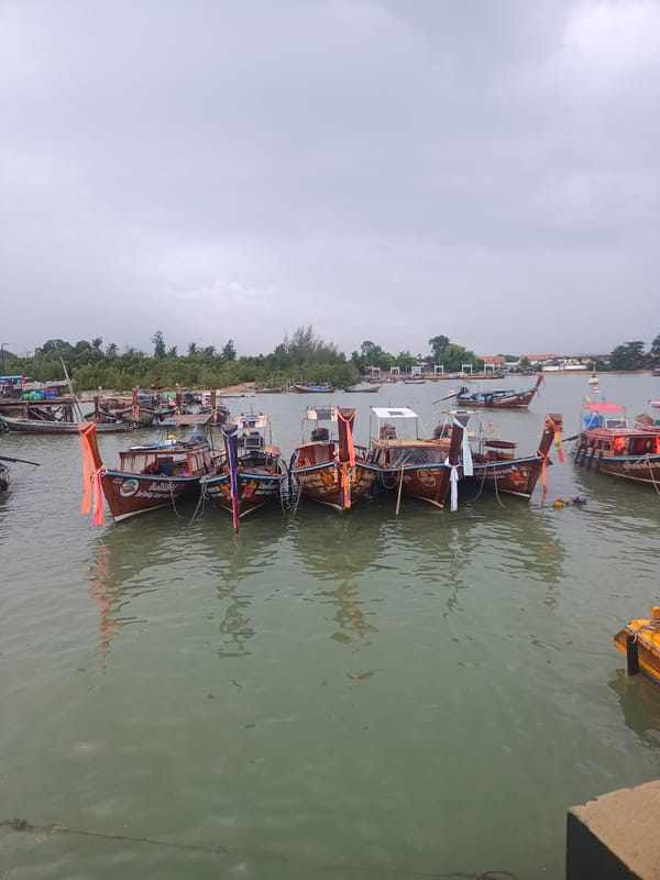 Traditional longtail boats dock at Thailand harbor under gray skies