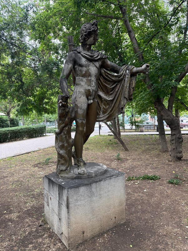 Dressed-up dogs roam a park near a classical bronze statue