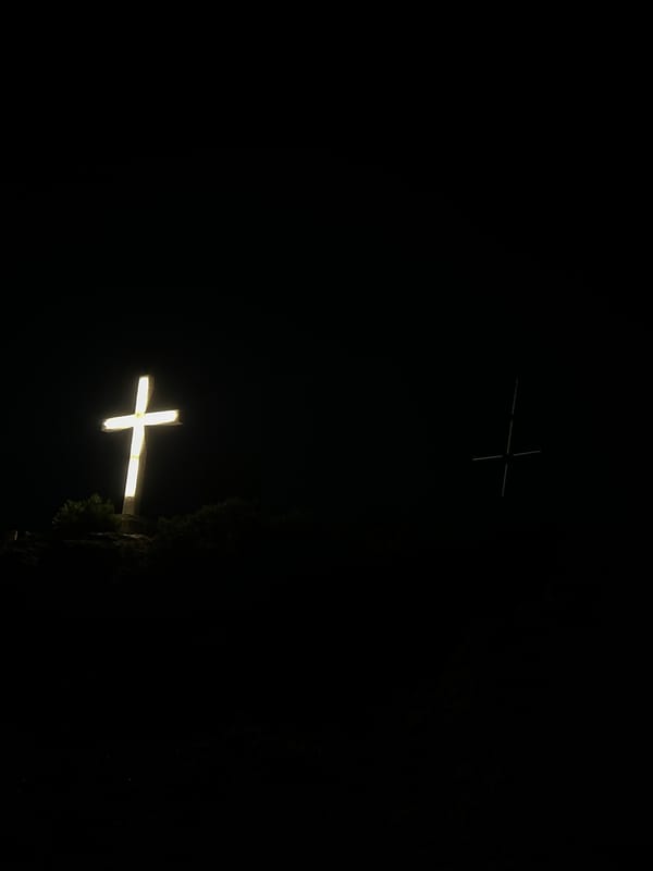 Illuminated hilltop cross overlooks a glowing coastal city at night