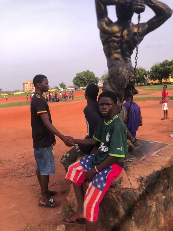 Young men play football near statue in Ukwu-Abwa, Nigeria