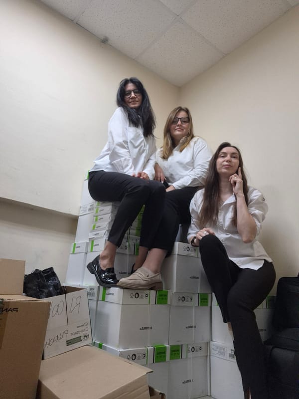 Three women pose playfully on labeled boxes indoors