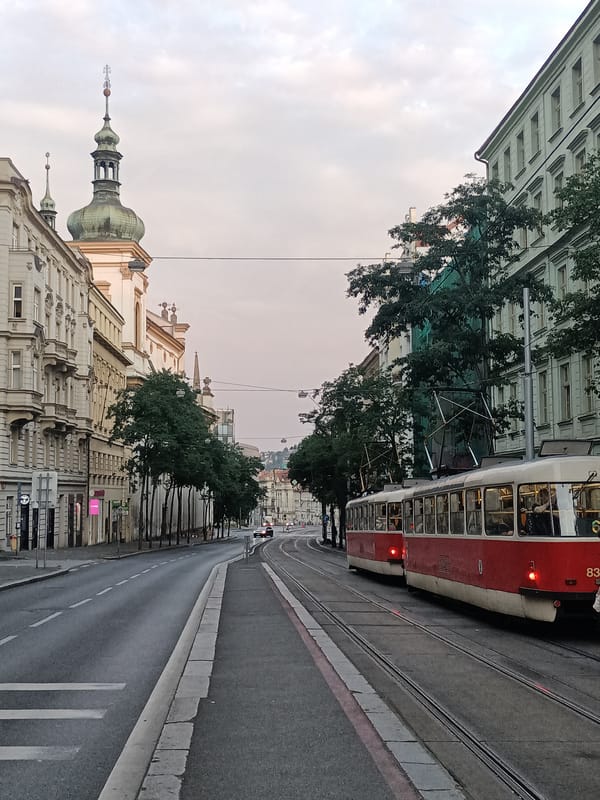Trams and traffic move through Prague's historic streets at dusk