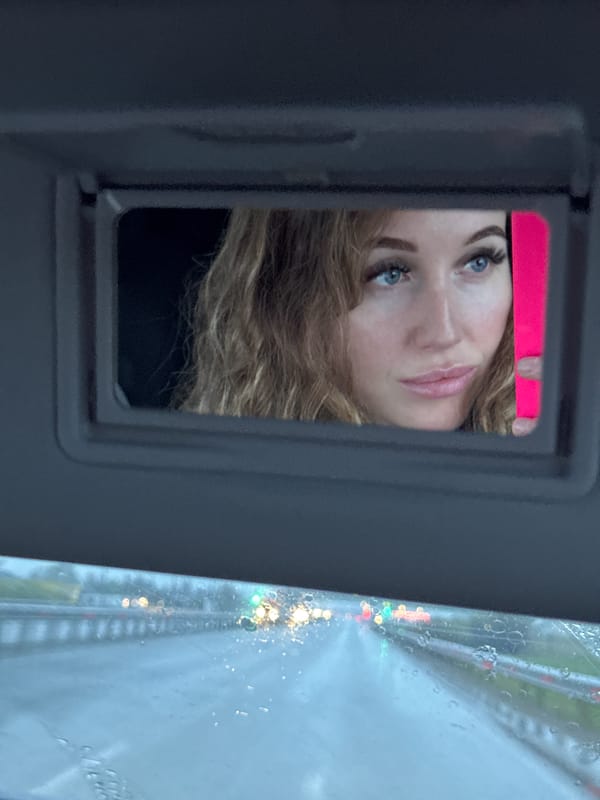 Woman uses car mirror with pink object in wet Russian town