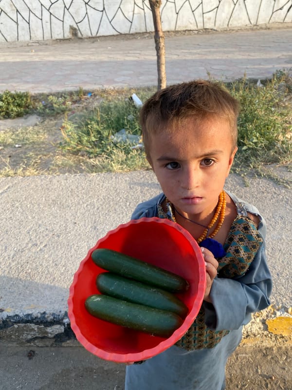 Child with orange bowl of cucumbers on a Kandahar path