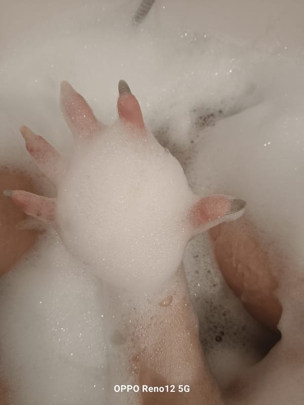Hand with dark nails photographed in foam-filled bathtub
