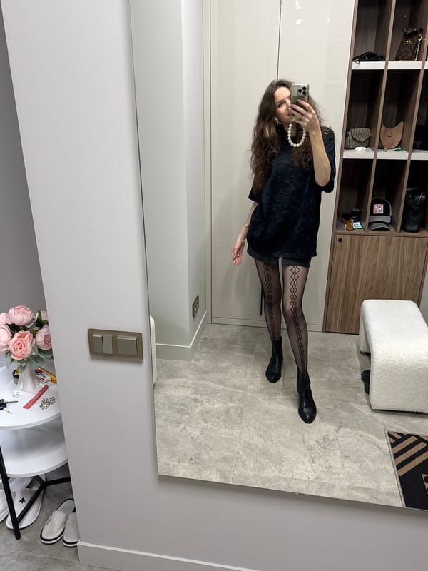 Person takes mirror selfie wearing black outfit and pearls