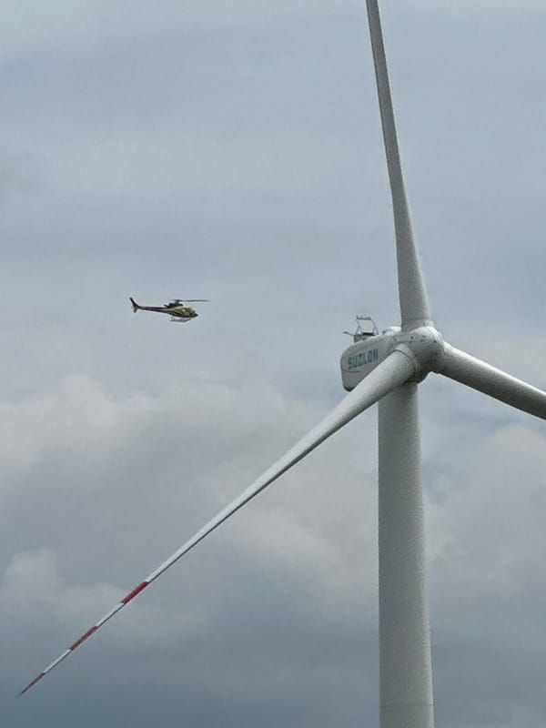 Yellow helicopter flies past wind turbine and comms tower in rural Ukraine