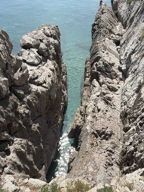 Person kneels on ledge overlooking water in Budva