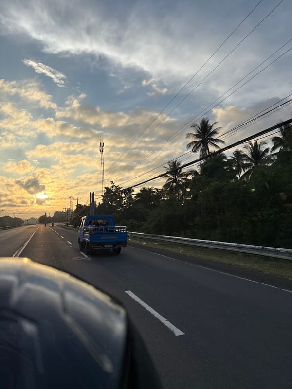 Blue pickup truck travels Philippine highway at sunset