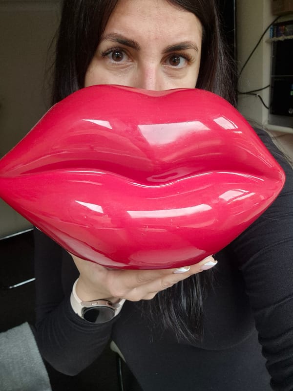 Woman poses playfully with giant red lips object in Suffolk