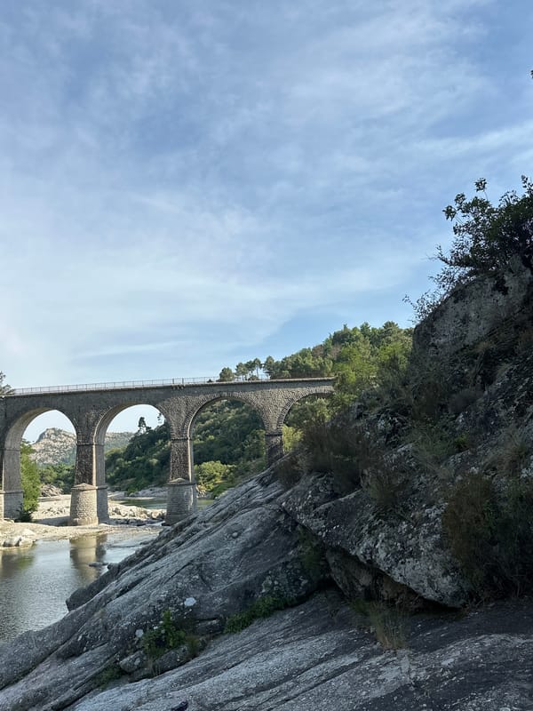 Stone viaduct over a clear green river through rocky forested terrain