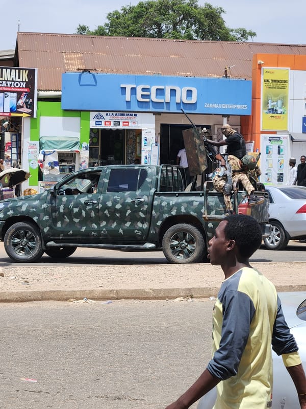 Military truck patrols urban street amid daily fruit vendors