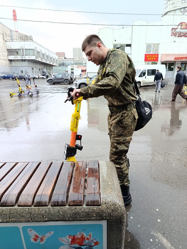 Military-clad man examines electric scooter on wet Moscow sidewalk