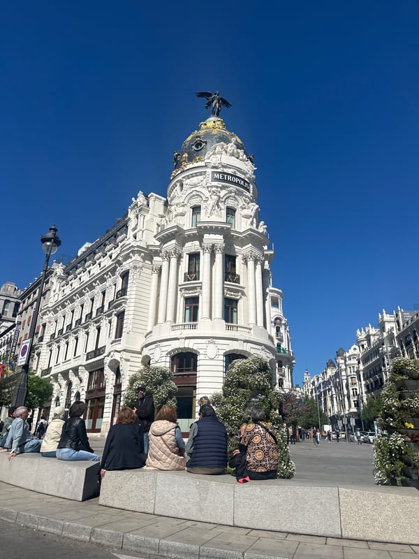 People gather near Madrid's historic Metropolis Building under clear skies